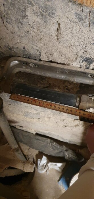 Ett skjutmått mot en stenmur, mäter avstånd, arbetsmiljö, verktyg synligt, sten, rör, och gammal isolering.