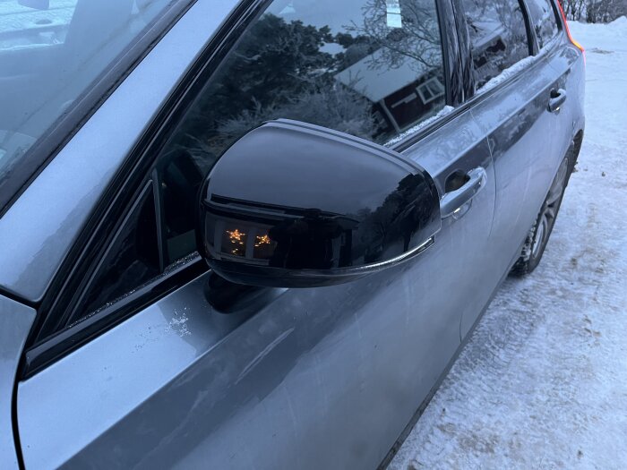 Grå bil parkerad i kallt väder, vintersäsong, med snörester, vid spegeln syns reflexion av ljus.