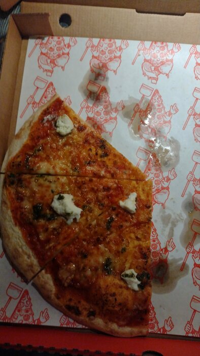 Delvis äten pizza i kartong med ostslices och tomatsås, mönster av dansande figurer på botten.