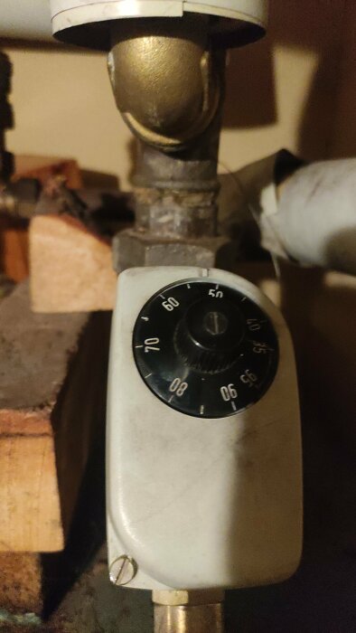 Termostatventil på radiator, temperaturinställningsratt, i en mörk miljö, åldrad och smutsig.