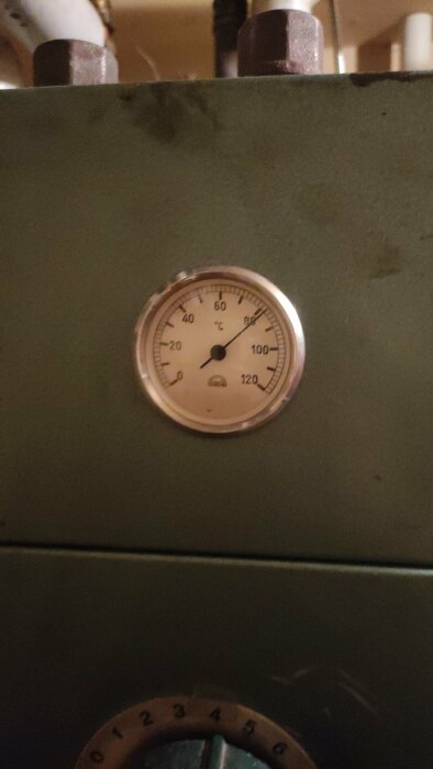 Termometer visar cirka 70 grader Celsius på en maskin eller utrustning.