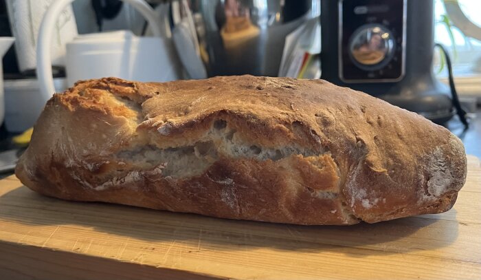 Nybakt bröd på skärbräda i kök, gyllenbrun skorpa, bakgrundsredskap suddiga.