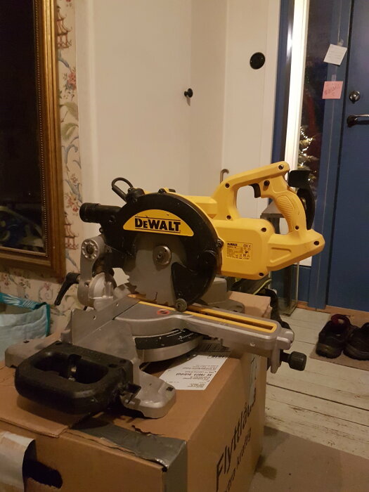 DeWalt kap- och geringssåg på kartong inomhus, arbetsverktyg, träarbete, gula och svarta färger, hemmiljö.