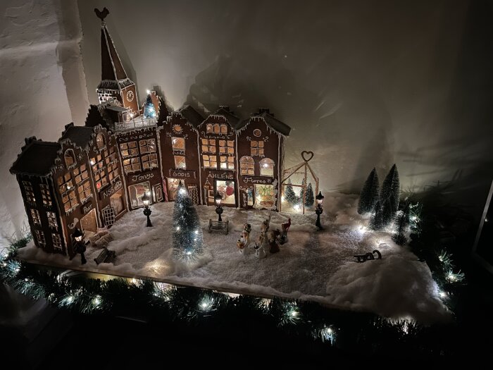 Modellby i vinterscen med belysta byggnader, träd, figurer och snö, skapar en julstämning.