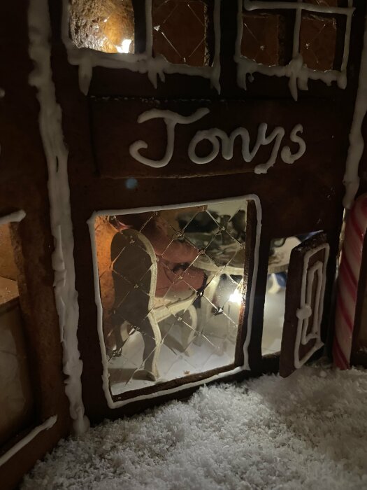 Pepparkakshus med namnet 'Tony's' skrivet, dekorativt isbildning, fönster och snö, mysig belysning inifrån.