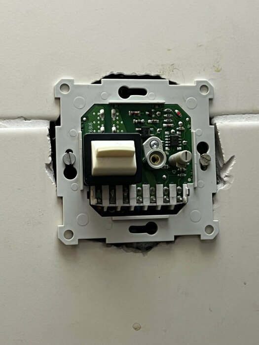 Elektrisk strömbrytare utan täckplatta, kretskort och mekanism syns, monterad på en vägg.