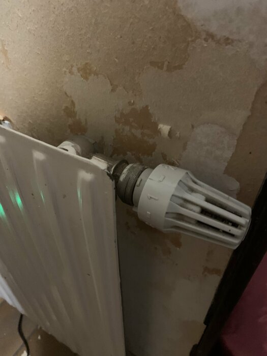 Radiator med termostatventil, flagnande färg på vägg, behov av renovering eller målning.