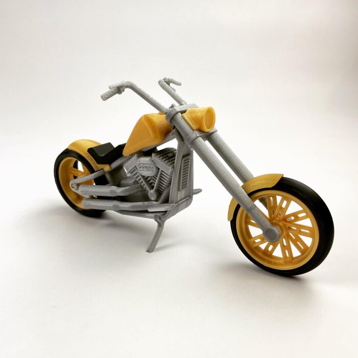 Modell av chopper-motorcykel med gula och gråa detaljer mot vit bakgrund.