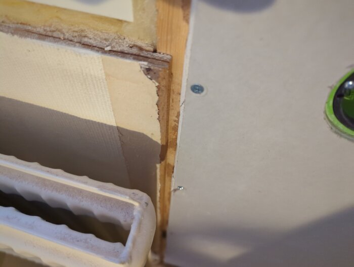 Vägg under konstruktion med synligt isoleringstejp, träregel, gipsskiva och en del av en radiator.