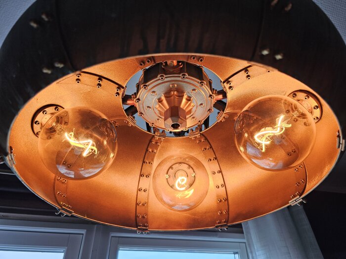 Industriell lampa med tre synliga glödlampor, koppar, hängande, reflekterar modern design och mysig atmosfär.