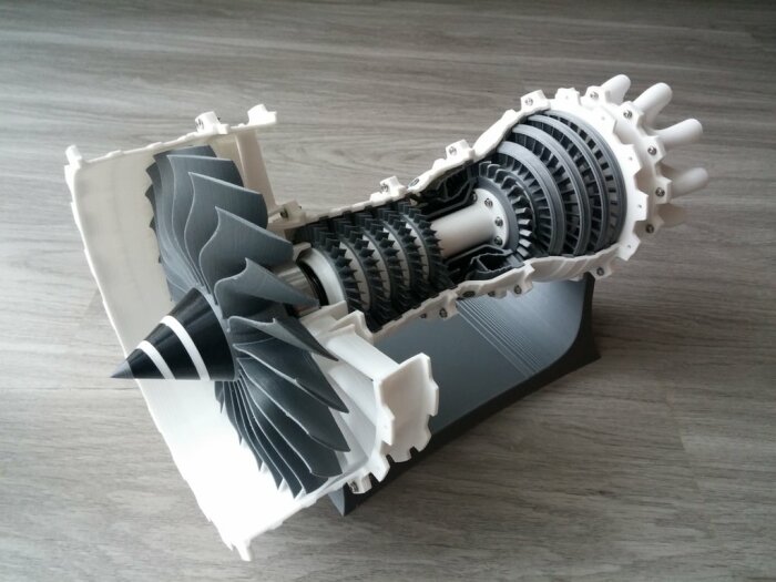 Modell av jetmotor, delvis sektionerad, visar inre komponenter och konstruktion, placerad på trägolv.