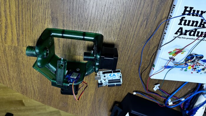En robotarm med servo och styrenhet, en bok om Arduino, kablar, på ett träbord.