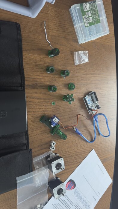 Bild av elektronikkomponenter, motorer, plastdelar och kretskort på ett bord, verkar vara DIY eller reparation.
