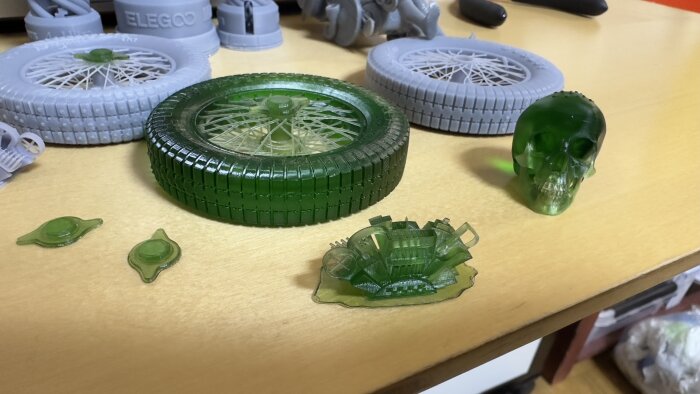 3D-utskrifter på ett bord, gröna genomskinliga och vita objekt, blandade former inklusive en dödskalle och däck.