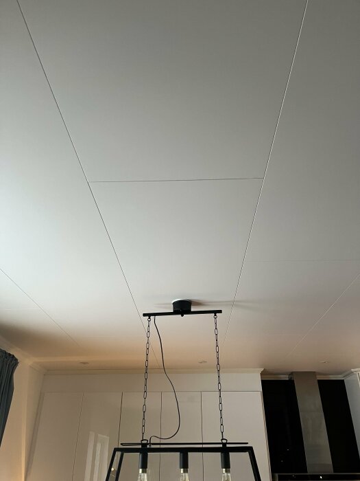 Taklampa med kedjor i ett modernt rum, vit takyta, dämpad belysning, minimalistiskt inrett.
