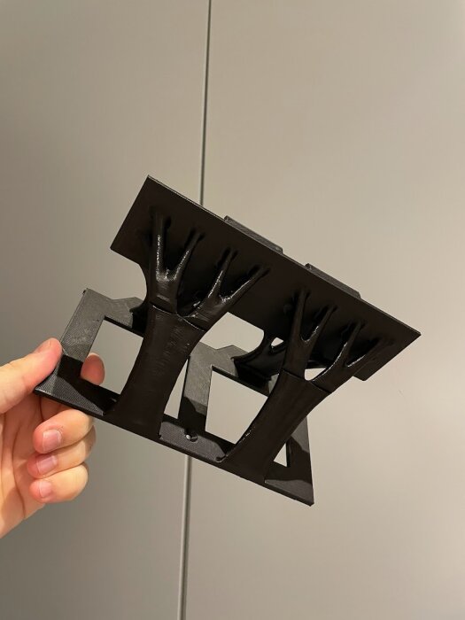 En hand håller en svart tredimensionell struktur som ser ut som flera upp och nedvända stolar sammanlänkade.