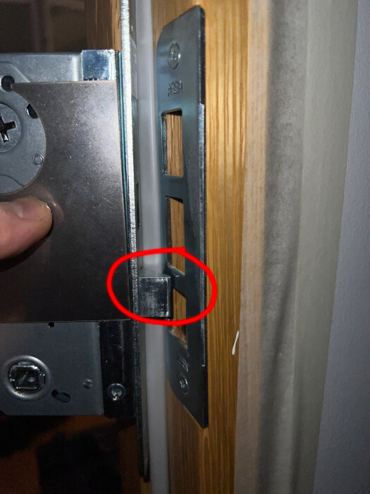Bilden visar delar av en dörr och karm, med fokus på en låsmekanism och dess passning.