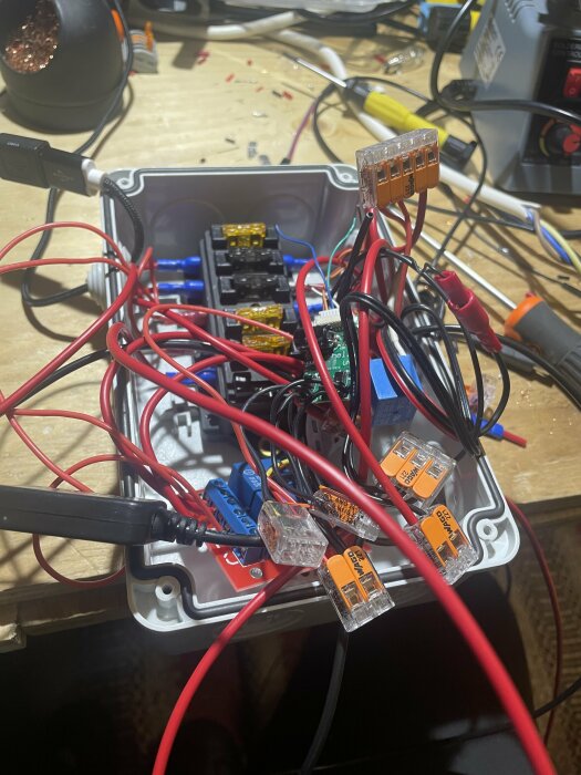 Elektronikprojekt med trassliga kablar, säkringar och kopplingsdon på en arbetsbänk.