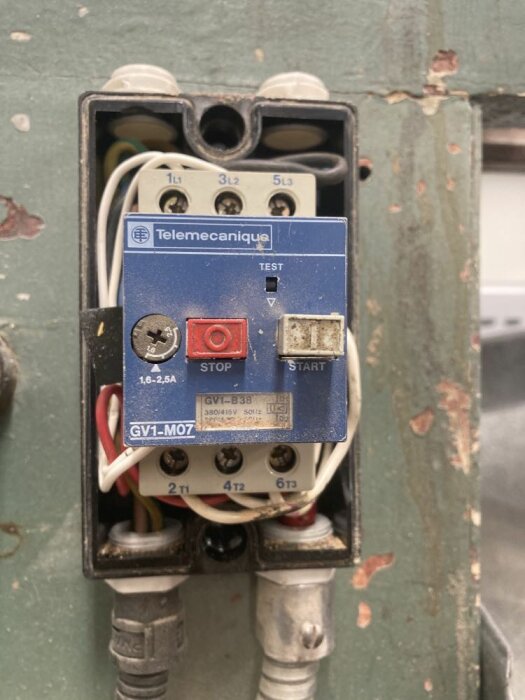 Ett öppet elektriskt panel med en motorstartare från Telemecanique, kopplingar och knappar för test, stopp, start.