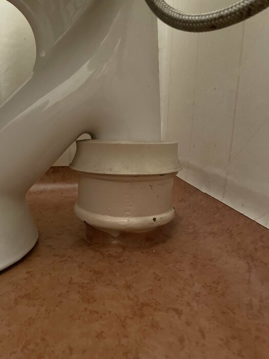 Toalettfot nära golv, keramik, kakel, rörledning, synlig fogmassa, beige-brunt golv.