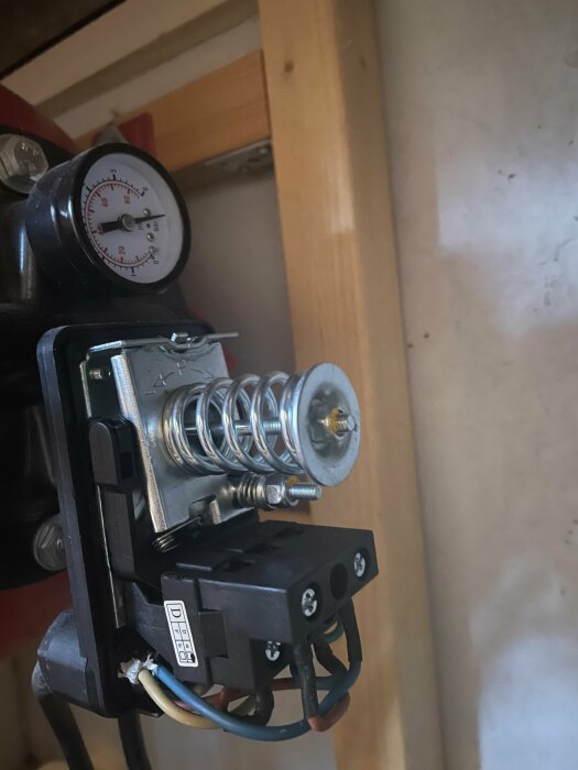 Tryckmätare, fjädrar och elektriska komponenter monterade på en träplatta inne i ett utrymme.