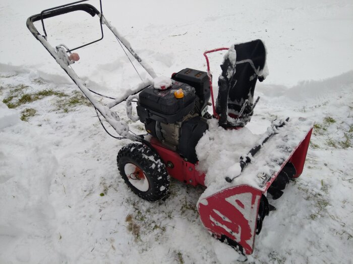 En röd snöslunga täckt med snö står på en snötäckt yta.