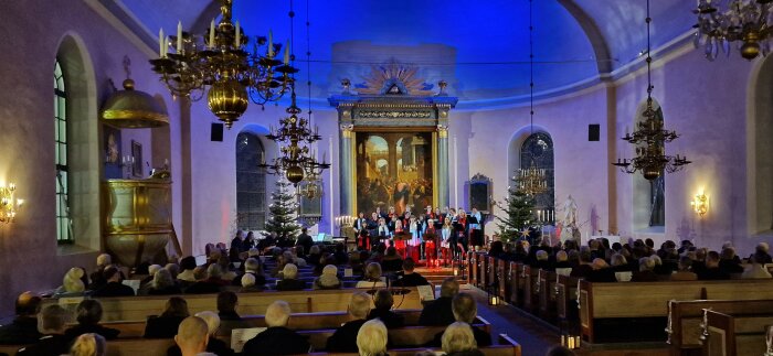 Kör uppträder i kyrka, publik tittar, julstämning, ljuskronor, julgranar, blå timmen, festligt.