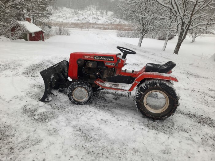 Röd traktor med snöslunga i ett vintrigt landskap med snö och träd.