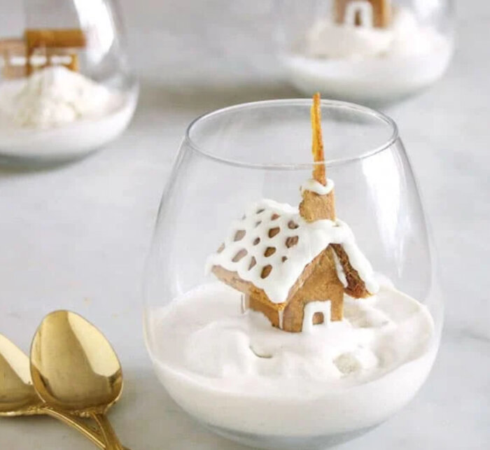 Ett pepparkakshus med "snö" i ett vinglas, kreativt dessertkoncept, festlig dekoration.