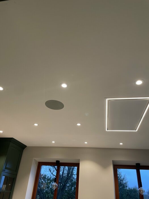 Modern inredning, infällda spotlights, rektangulär LED-list, fönster mot trädbakgrund, hänglampa, strömlinjeformat kök.