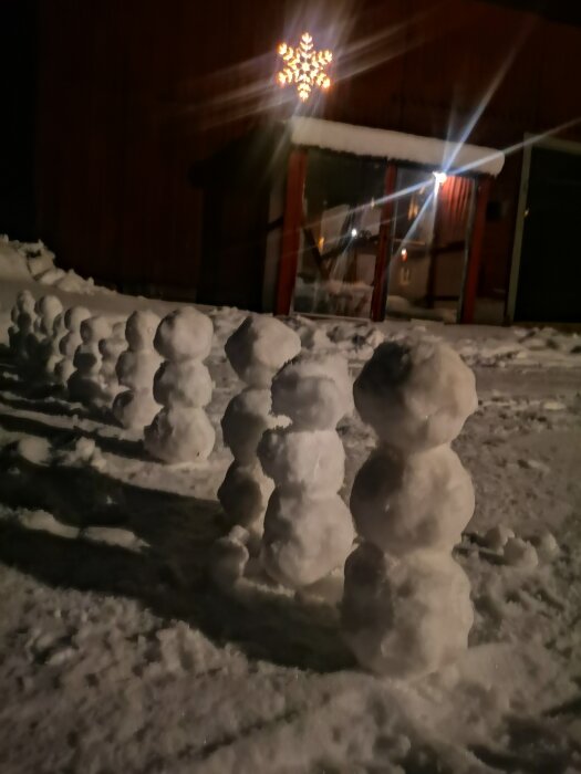 Rad av ojämna snöbollar på nattlig yta, träbyggnad i bakgrunden, julstjärna lysande ovanför.