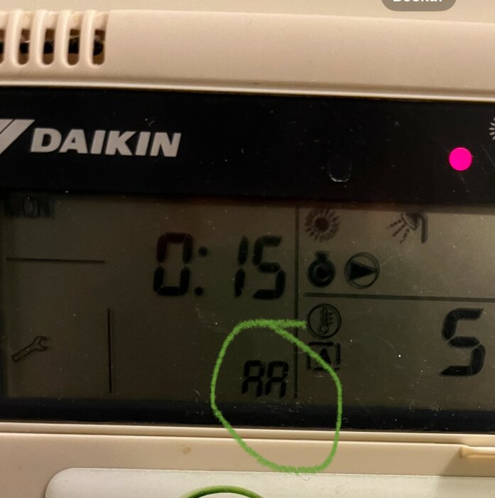 Digitalklocka visar 00:15, omringad symbol "RR" på termostat. Daikin-varumärke, rosa markör uppe till höger.