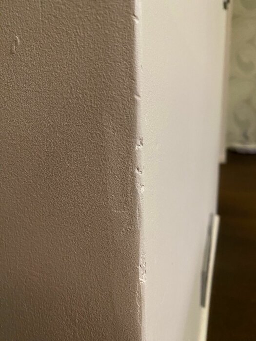 En närbild på en vitmålad väggkant med små skador och avflagningar vid ett hörn.