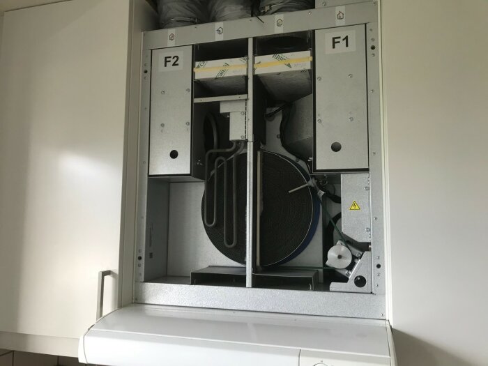 Öppen ventilationsskåp med filter och mekaniska delar synliga i ett ljust rum.