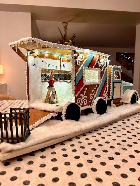 Pepparkakståg med dekorativ glasyr, uppställt på bord med snöliknande underlag och små prickar. Festlig, kreativ juldekoration.