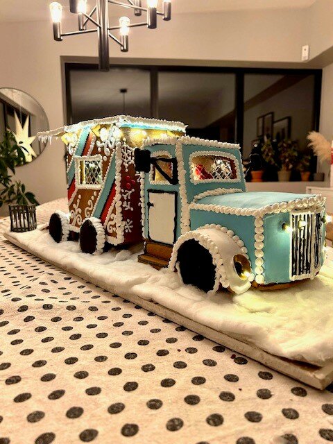 Pepparkakshus formad som en lastbil och husvagn med julbelysning, står på ett bord.