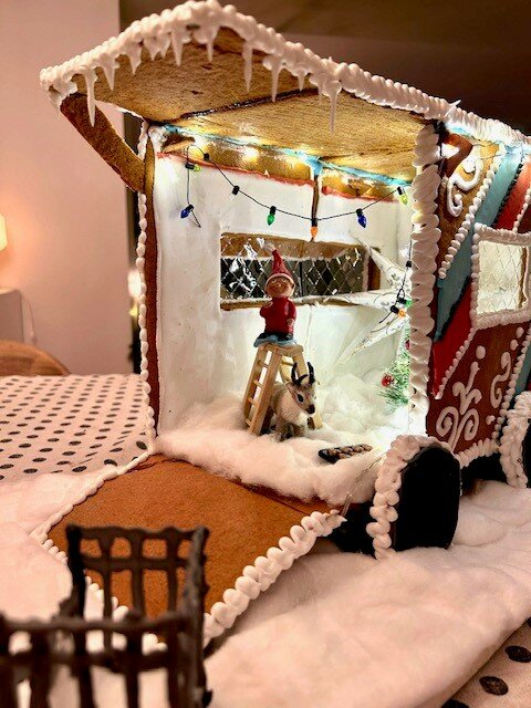 Pepparkakshus med julbelysning, snögubbe, istappar och figur på stege. Dekorativt, festligt, julstämning, inomhus.