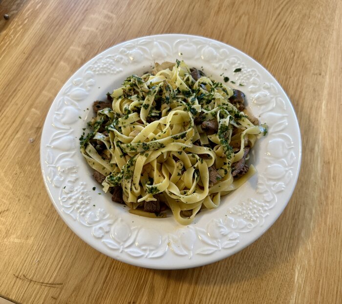 En tallrik med pasta tagliatelle, kött och gröna örter på ett träbord. Nylagad och aptitretande.