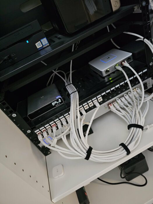 Nätverksskåp med switch, patchpanel, kablar, strömförsörjning och kommunikationsutrustning på hyllor.