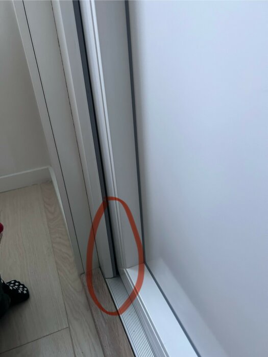 Dörr, golv, vägg, röd cirkel markerar specifik del, sko syns delvis.