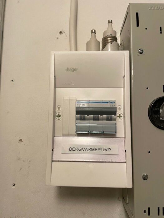 Elcentral med säkringar och etiketten "BERGVÄRMEPUMP" på en vägg, bredvid en grå elbox.