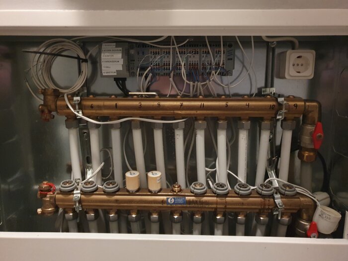 Uppmärkt värmefördelare med rör, termostater och kopplingar för golvvärmesystem inomhus.