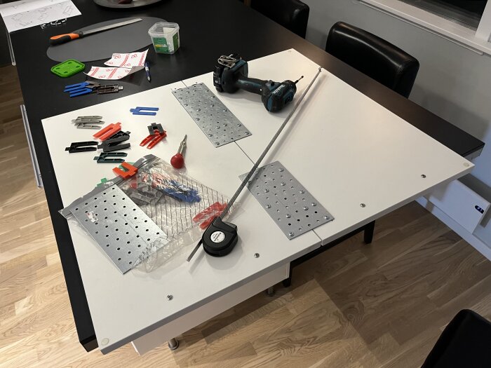 Ett vitt bord med DIY-verktyg och -material för ett monteringsprojekt i ett hemmakontor.