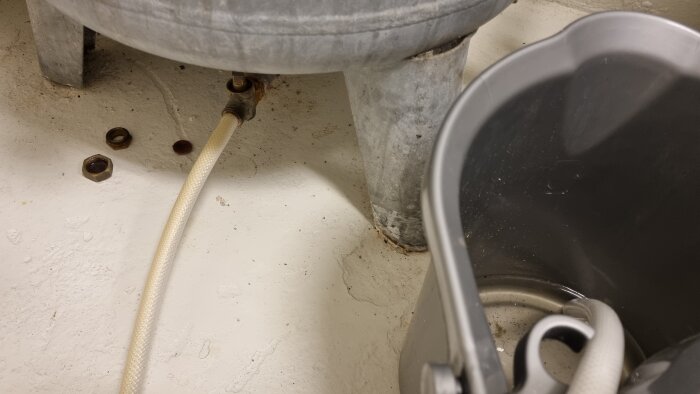 Pedestal sink with detached pipes, screws on floor, bucket collecting possible leakage.