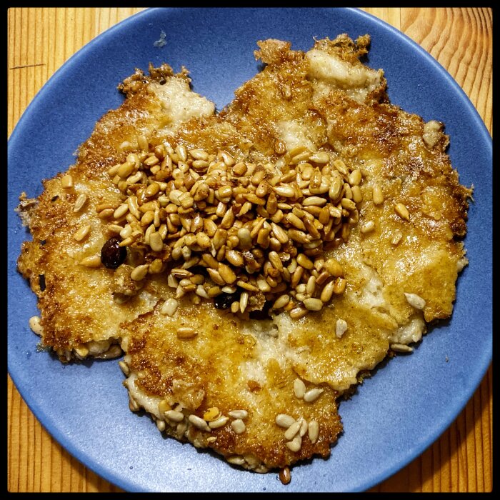 Panerad schnitzel med stekt solrosfrön på blå tallrik, träbakgrund.