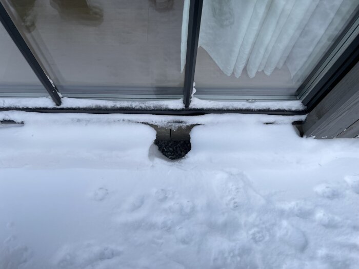 Fönsterdörr med öppen glidmekanism delvis täckt av snö och underlag av grus.