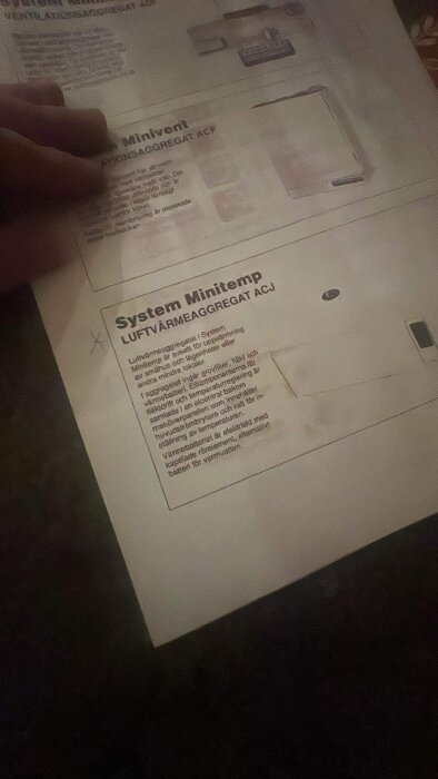 En hand håller ett informationsblad om luftvärmesystemet 'System Minitemp' med teknisk text på svenska.