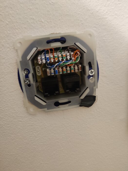 Öppen nätverksuttagsdosa med exponerade kablar och kontakter monterade på en vägg.
