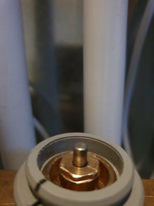 Närbild på ett rundat objekt med metallstift, eventuellt en del av en apparat eller maskin. Oskarpt i bakgrunden.