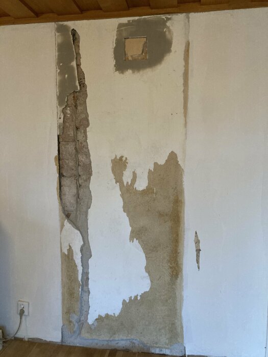 Skadad vägg med fuktproblem, avskalad färg och puts, synlig elinstallation, repareringsbehov.